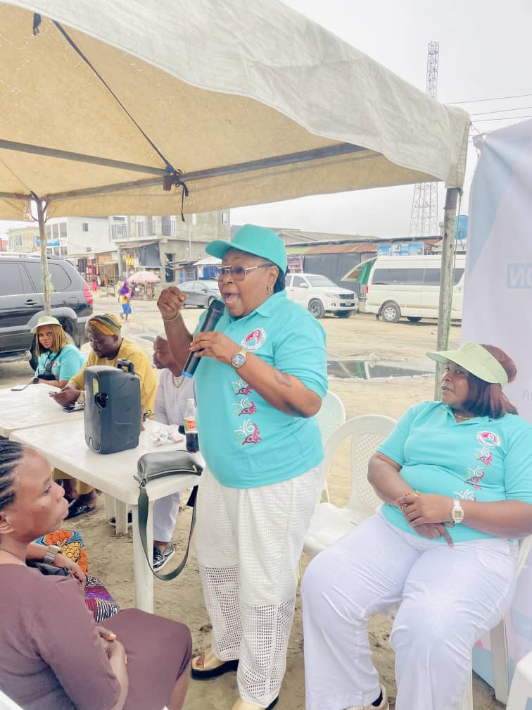 A community elder addressing residents with a microphone under a canopy